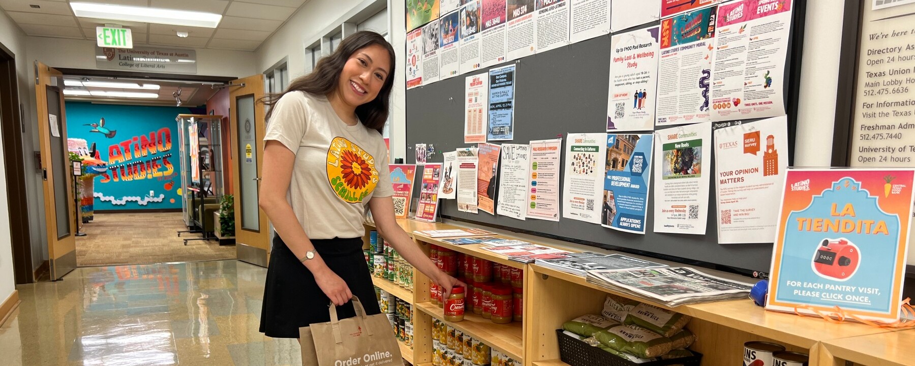 A student smiles while grabbing a jar of peanut butter from "La Tiendita" free student pantry.