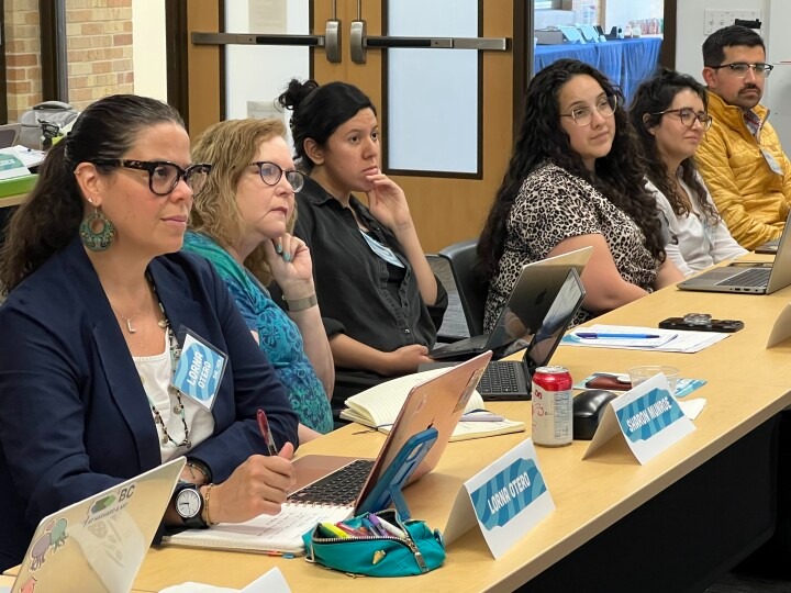 Scholars at the annual Summer Doctoral Institute listen to a lecture with their laptops and notebooks on the desk in front of them.