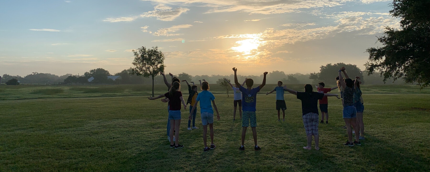 Image of Camp Shakespeare students in a circle in a field at sunrise.