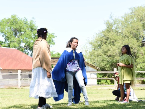 image of three performers outside, one wearing a big blue cloak